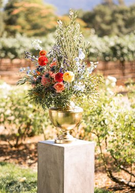 Gorgeous accent flowers to frame the ceremony location at the Harvest Inn in Napa County. Pops of orange, coral, yellow, and a hint of blue flowers, with olive leaves as greenery. Love the vineyards fading into the distance! Thanks to Maria Villano Photography and Beijaflor Botanicals for their creativity! 